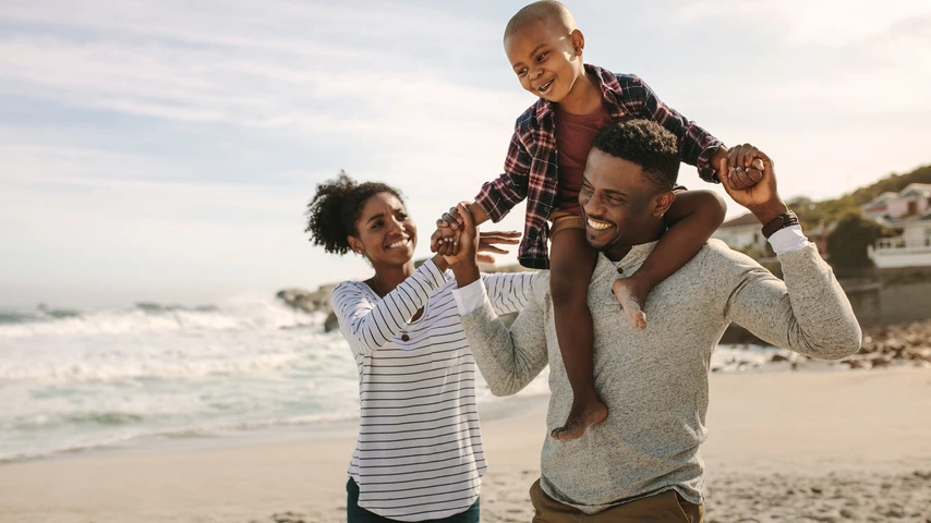 Parents carrying son on shoulders on beach vacation. African family of mother and father carrying son on his shoulders on vacation.